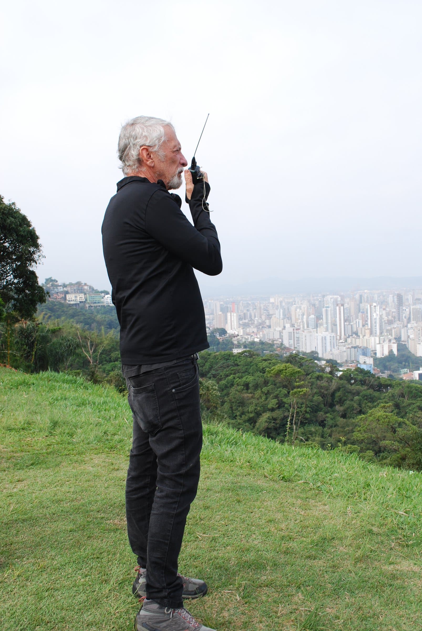 Eladio em pé na rampa, de perfil, falando ao rádio com um aluno em voo