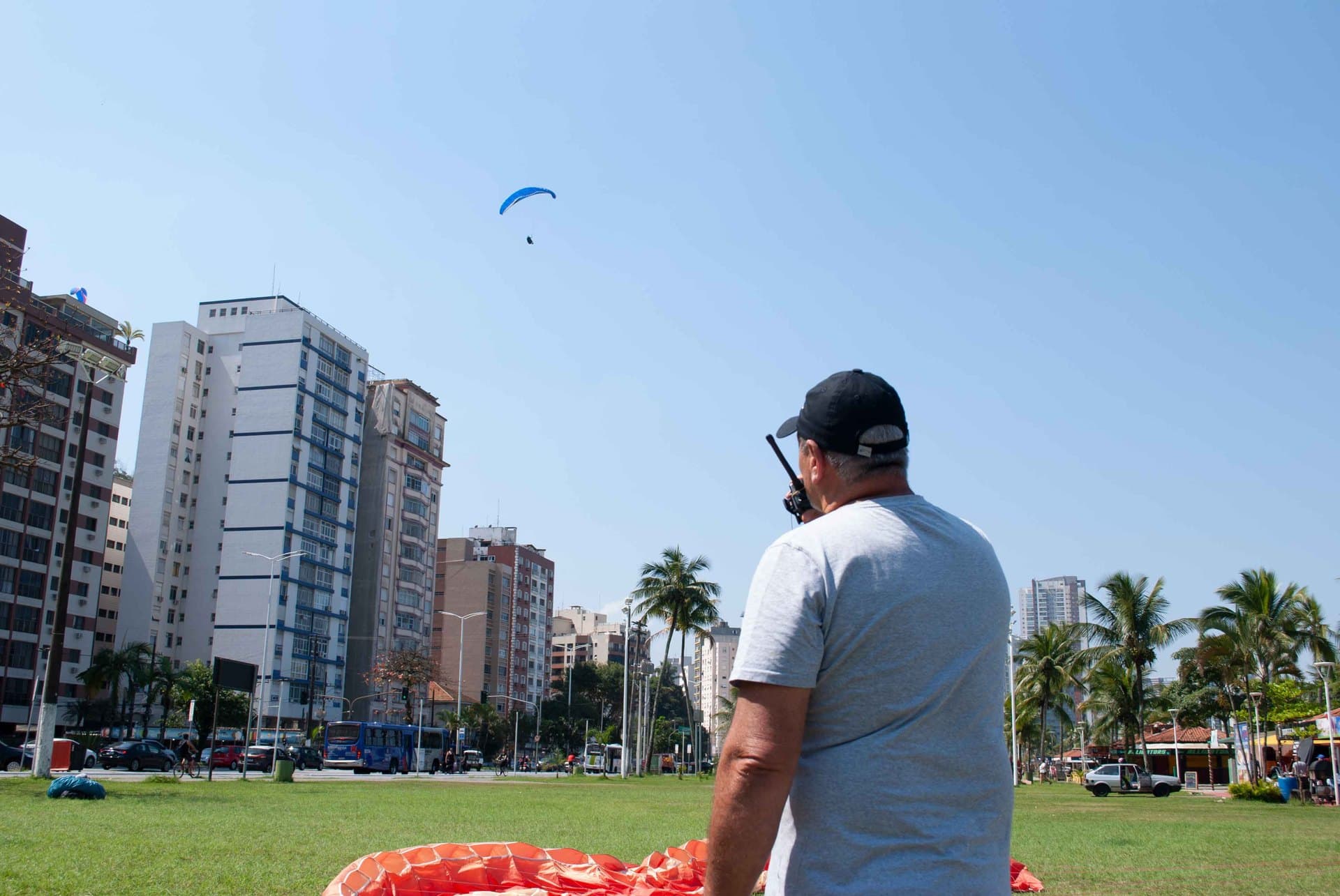 Instrutor de costas, com o rádio na mão, acompanha a aproximação de um parapente para o pouso