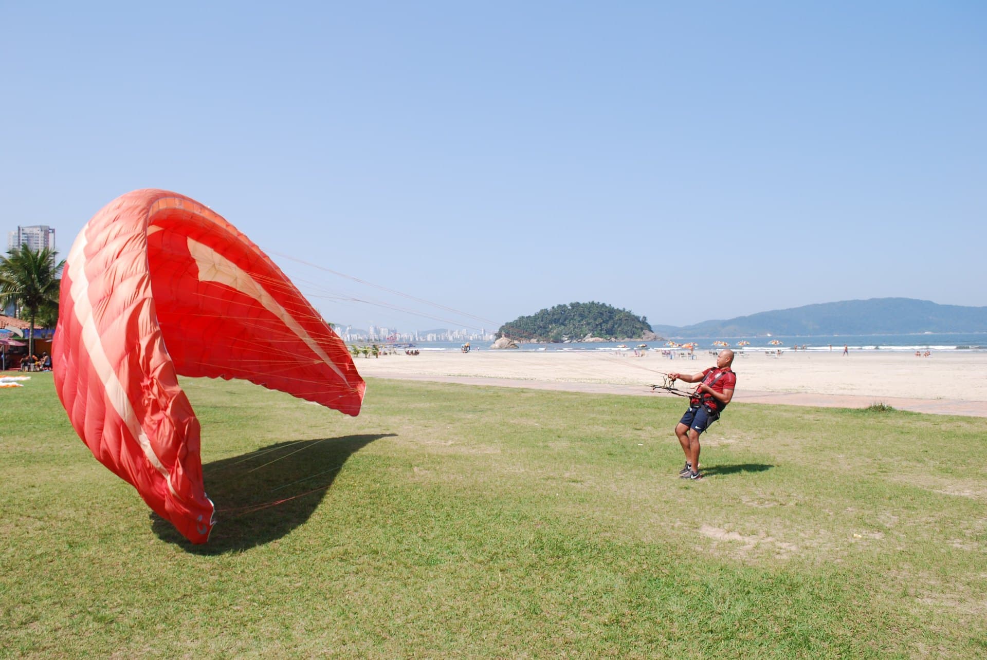 Aluno infla uma vela vermelha no gramado de treino, de frente para a praia do Itararé e a ilha Porchat